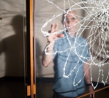 Artist portrait of a man seen through a glass panel painted with abstract white line work