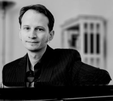 Black and white portrait of a man resting his arms on a grand piano