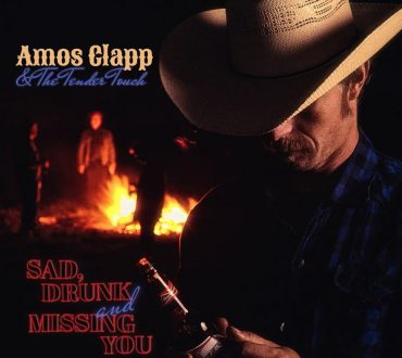 Album cover portrait of a musician in a cowboy hat by firelight, holding a beer bottle