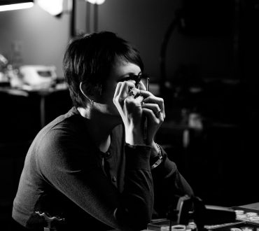 Black and white environmental portrait of a woman examining a small object at a jeweler's workbench