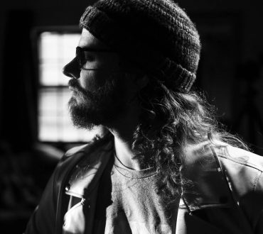 Black and white profile portrait of a bearded man with long hair in dramatic window light