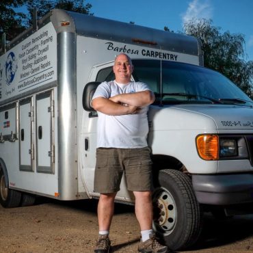 Environmental portrait of a contractor standing with arms crossed in front of a branded work van