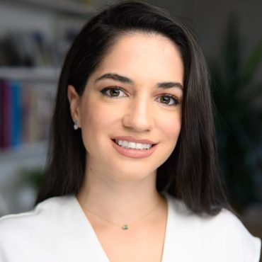 Close-up business headshot of a woman in a white blouse against a blurred office background