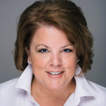 Close-up studio headshot of a woman in a white shirt against a gray background