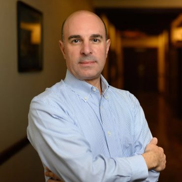 Environmental business portrait of a man with arms crossed in a warmly lit office corridor