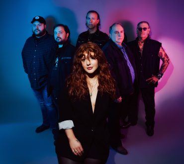 Band portrait of six musicians against a blue and purple gradient studio backdrop